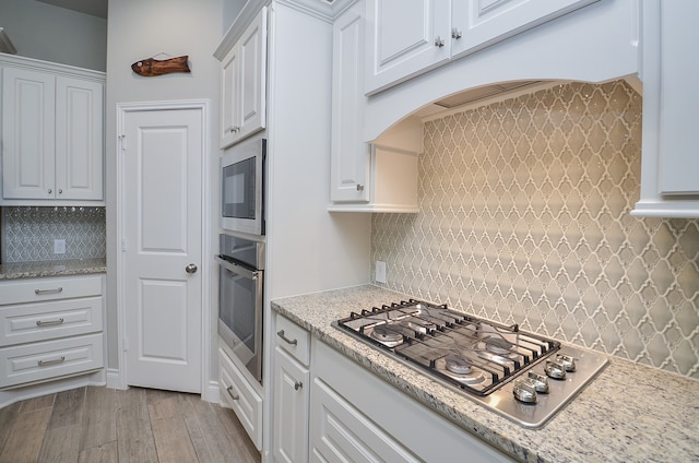 kitchen with light stone countertops, white cabinetry, light hardwood / wood-style floors, stainless steel appliances, and decorative backsplash