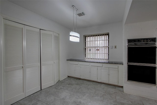 kitchen with visible vents, dark stone counters, dobule oven black, white cabinetry, and decorative light fixtures