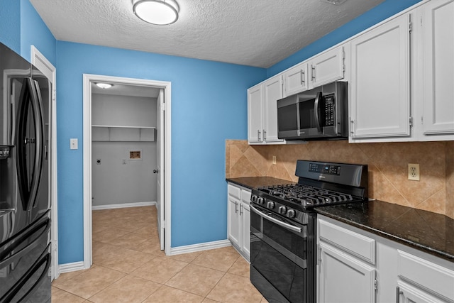 kitchen featuring backsplash, dark stone counters, light tile patterned floors, appliances with stainless steel finishes, and white cabinetry