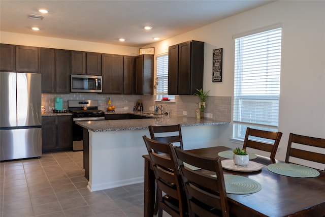 kitchen featuring kitchen peninsula, decorative backsplash, stainless steel appliances, and light stone counters