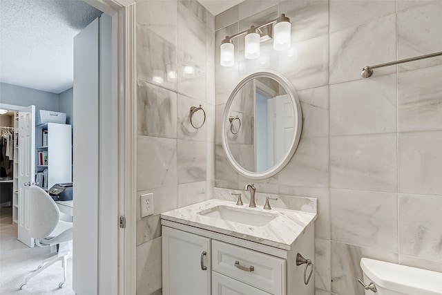 bathroom featuring toilet, a textured ceiling, vanity, and tile walls