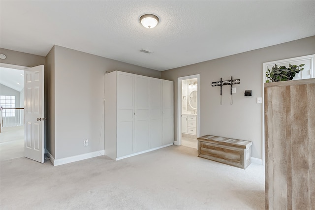 unfurnished bedroom with connected bathroom, light carpet, and a textured ceiling