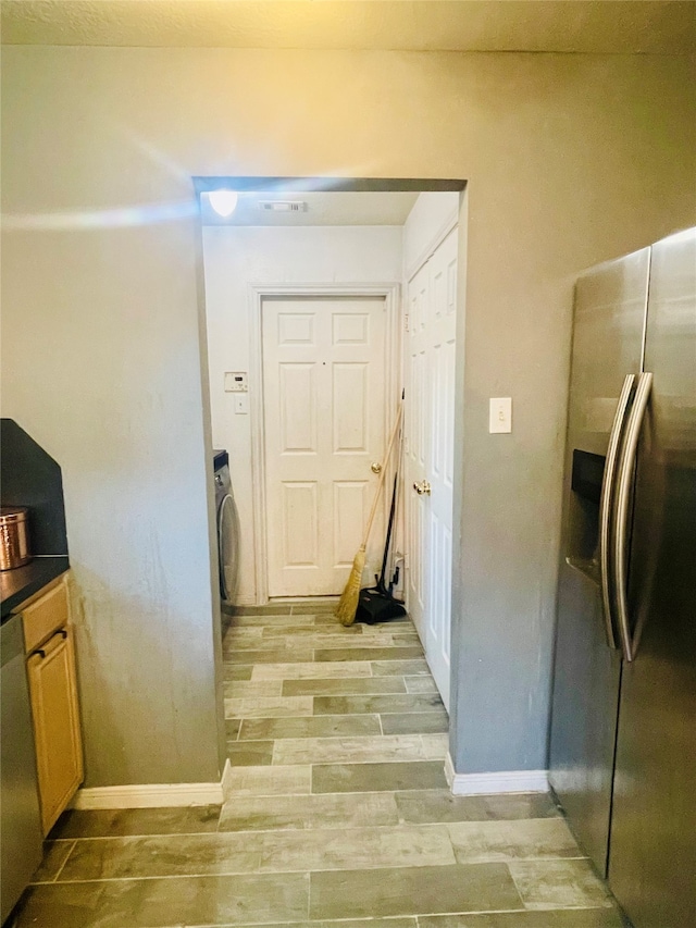 interior space featuring washer / dryer, light hardwood / wood-style flooring, and stainless steel refrigerator with ice dispenser