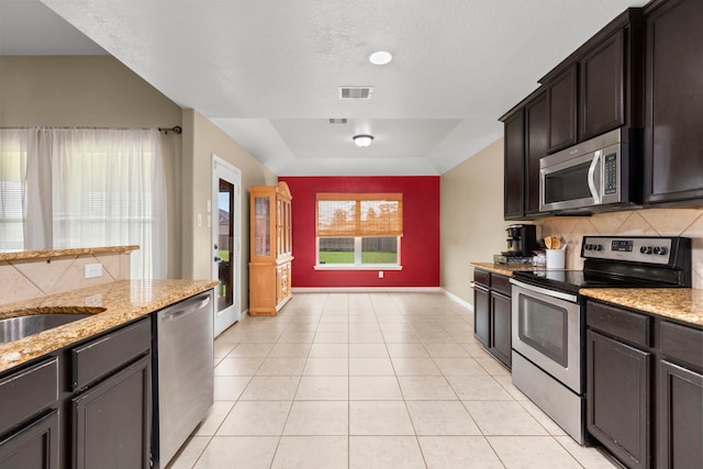 kitchen with light stone countertops, dark brown cabinetry, stainless steel appliances, and light tile patterned floors