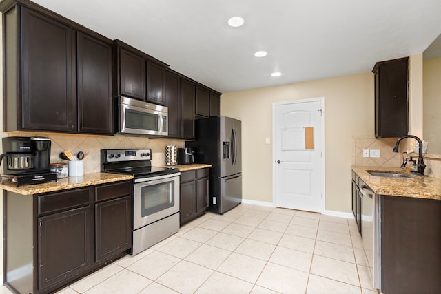 kitchen with sink, stainless steel appliances, light stone counters, backsplash, and dark brown cabinets