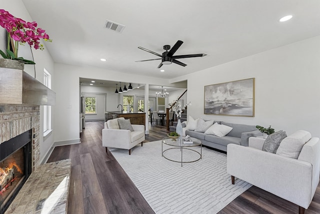 living room featuring sink, a brick fireplace, dark hardwood / wood-style floors, and ceiling fan with notable chandelier