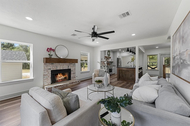 living room with sink, a fireplace, wood-type flooring, and ceiling fan