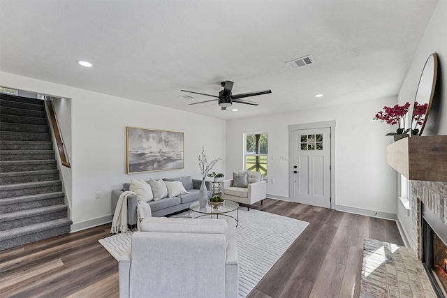 living room with ceiling fan, a textured ceiling, dark hardwood / wood-style flooring, and a brick fireplace