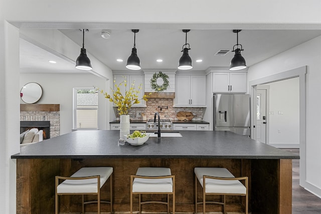 kitchen featuring a large island with sink, sink, white cabinets, and stainless steel refrigerator with ice dispenser