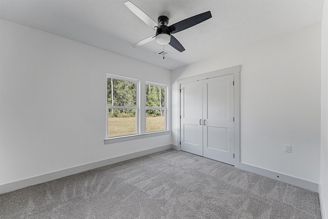 unfurnished bedroom featuring a closet, a textured ceiling, light colored carpet, and ceiling fan