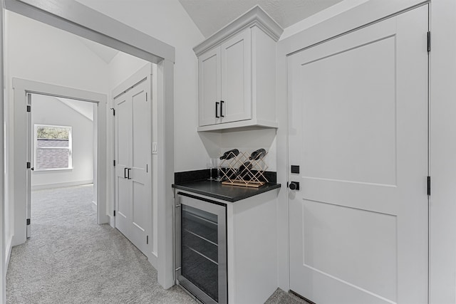 bar with a textured ceiling, white cabinetry, vaulted ceiling, wine cooler, and light colored carpet