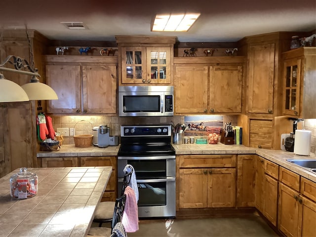 kitchen with tile countertops, decorative backsplash, and stainless steel appliances