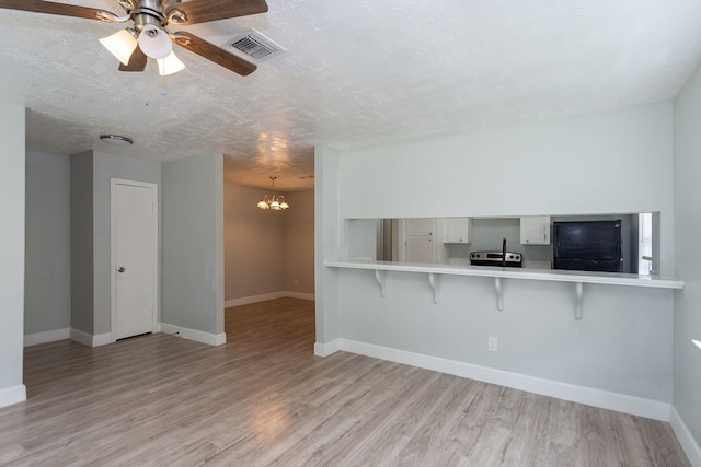 interior space with light wood-type flooring, ceiling fan with notable chandelier, and a textured ceiling