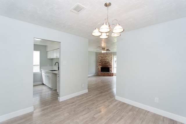 unfurnished dining area with a large fireplace, ceiling fan with notable chandelier, light hardwood / wood-style floors, and a textured ceiling