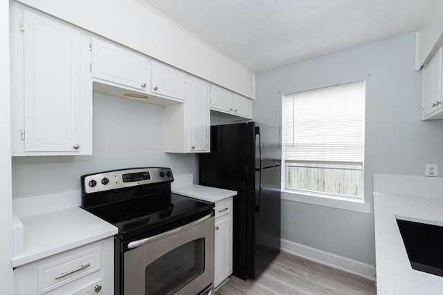 kitchen featuring stainless steel electric range, black fridge, light stone counters, light wood-type flooring, and white cabinets