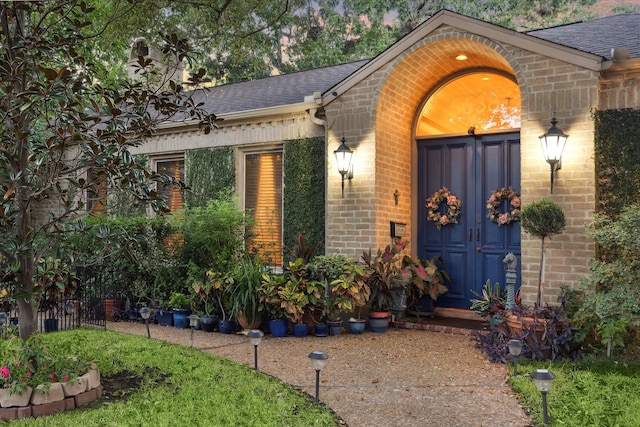 entrance to property with a shingled roof and brick siding