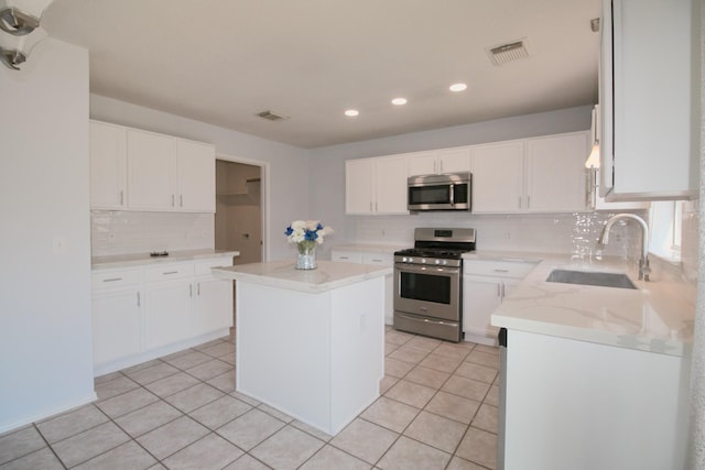 kitchen with appliances with stainless steel finishes, sink, light tile patterned floors, white cabinets, and a center island