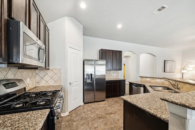 kitchen with decorative backsplash, dark brown cabinets, light stone counters, appliances with stainless steel finishes, and sink