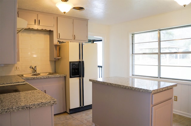 kitchen featuring decorative backsplash, light stone countertops, sink, a center island, and white refrigerator with ice dispenser