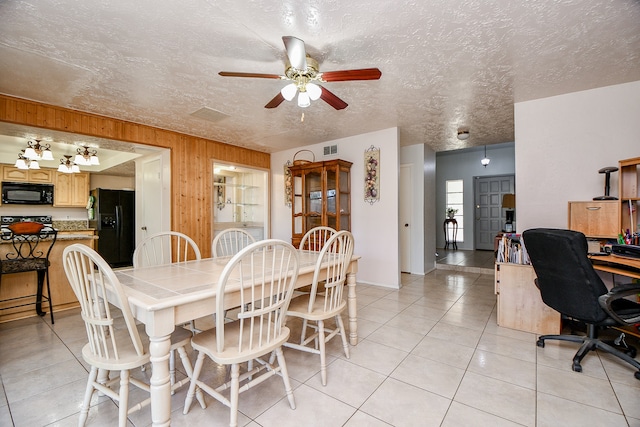 tiled dining space with a textured ceiling, ceiling fan, and wood walls