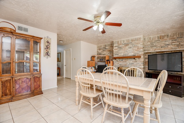 tiled dining area featuring ceiling fan, a textured ceiling, and a brick fireplace