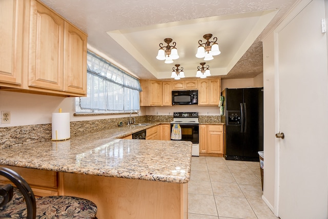 kitchen with kitchen peninsula, light brown cabinetry, light stone counters, a tray ceiling, and black appliances