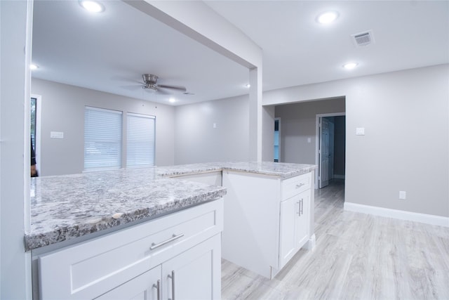 kitchen with light stone countertops, white cabinetry, and ceiling fan