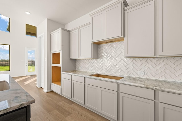 kitchen with light hardwood / wood-style floors, light stone counters, sink, and tasteful backsplash