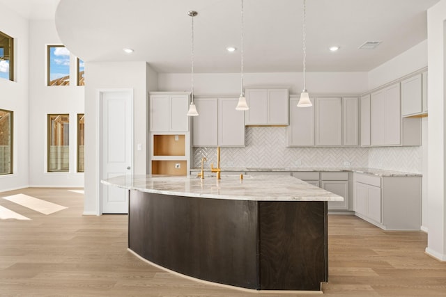 kitchen featuring light stone countertops, decorative light fixtures, light hardwood / wood-style floors, and a kitchen island with sink