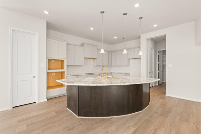 kitchen with light stone countertops, light wood-type flooring, an island with sink, and tasteful backsplash