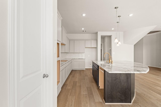 kitchen with sink, hanging light fixtures, light hardwood / wood-style flooring, an island with sink, and white cabinetry