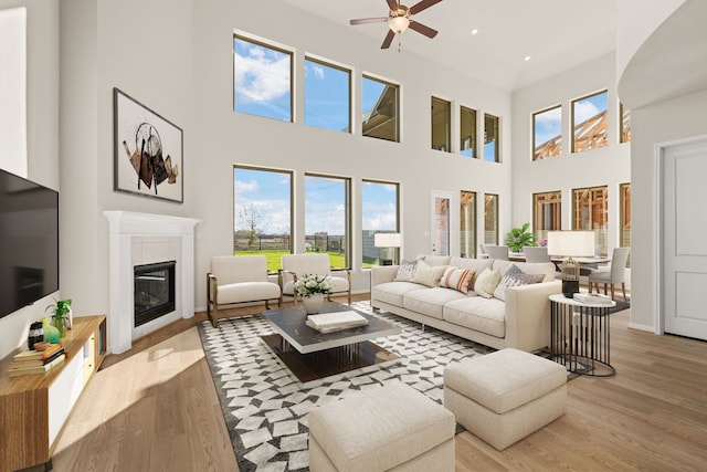 living room featuring ceiling fan, a fireplace, a towering ceiling, and light hardwood / wood-style floors