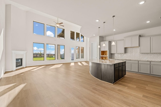 kitchen featuring gray cabinetry, a center island with sink, light wood-type flooring, and hanging light fixtures