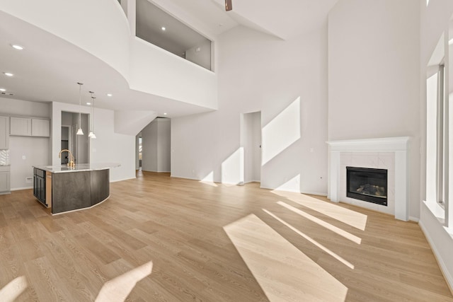 unfurnished living room featuring beverage cooler, light wood-type flooring, a tile fireplace, and a towering ceiling