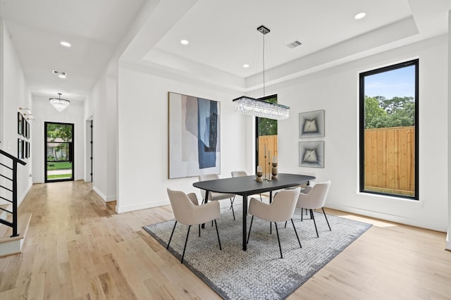 dining area with a healthy amount of sunlight, a raised ceiling, light wood-type flooring, and a chandelier