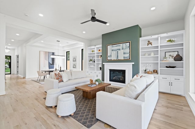 living room featuring light wood-type flooring, a raised ceiling, and ceiling fan