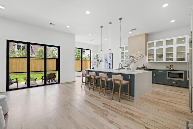 kitchen with gray cabinetry, stainless steel microwave, tasteful backsplash, a kitchen breakfast bar, and decorative light fixtures