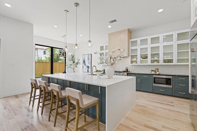 kitchen featuring a breakfast bar, stainless steel microwave, an island with sink, and hanging light fixtures