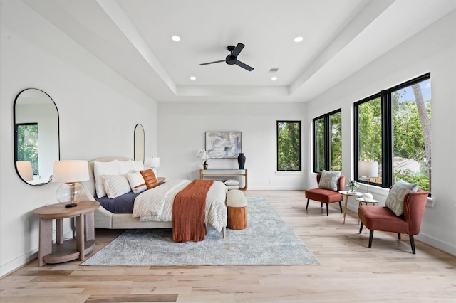 bedroom with ceiling fan, a raised ceiling, and light hardwood / wood-style flooring