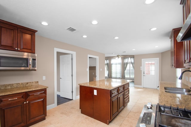 kitchen with light stone countertops, sink, a kitchen island, ceiling fan, and stainless steel appliances