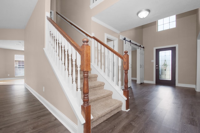 foyer featuring a towering ceiling, crown molding, a barn door, and dark hardwood / wood-style flooring