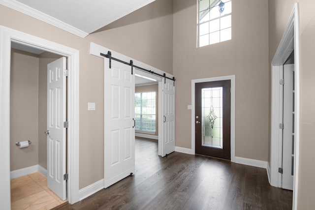 entrance foyer with a towering ceiling, ornamental molding, a barn door, and dark wood-type flooring