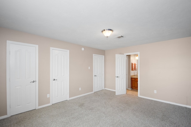 unfurnished bedroom featuring light carpet and connected bathroom