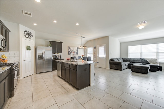 kitchen featuring a center island with sink, light stone counters, backsplash, appliances with stainless steel finishes, and sink