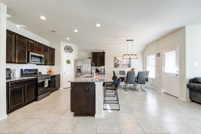 kitchen with light stone countertops, appliances with stainless steel finishes, an island with sink, decorative backsplash, and a breakfast bar