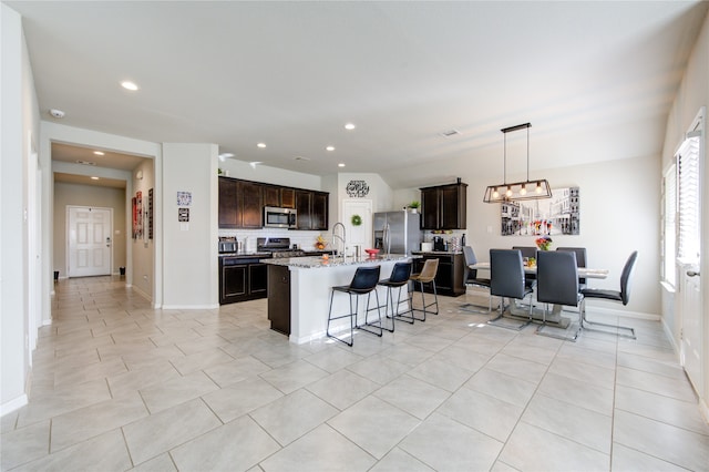 kitchen featuring tasteful backsplash, an island with sink, stainless steel appliances, dark brown cabinetry, and light stone counters