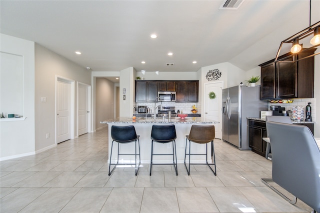 kitchen featuring tasteful backsplash, appliances with stainless steel finishes, light tile patterned flooring, dark brown cabinetry, and a center island with sink