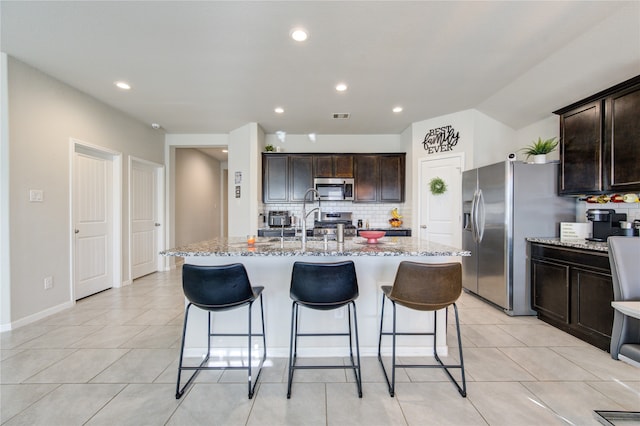 kitchen featuring dark brown cabinets, tasteful backsplash, stainless steel appliances, and a center island with sink