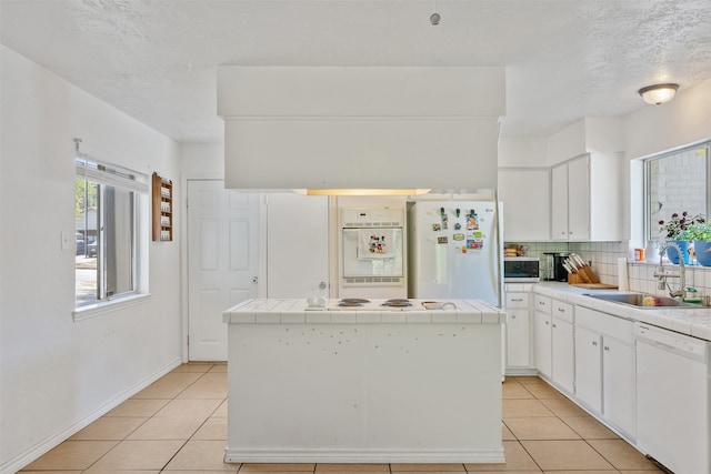 kitchen featuring decorative backsplash, tile counters, white cabinets, and white appliances