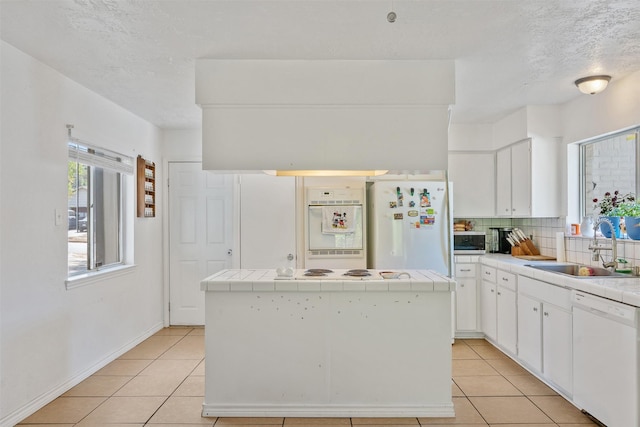 1603 Cantrell Blvd, Conroe, TX 77301 - kitchen with white appliances, tile countertops, a sink, light tile patterned floors, and a textured ceiling